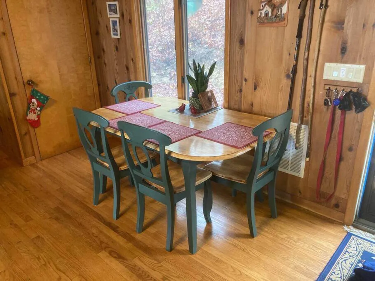 A bright dining area with a wooden table, blue chairs, and red placemats, set in front of a large window that fills the space with natural light. The setting exudes warmth and invites both meals and casual gatherings.