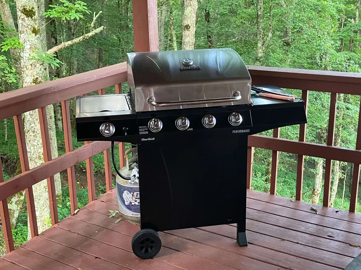 A spacious deck surrounded by lush greenery, featuring a grill and outdoor dining setup. The area is ideal for family barbecues or relaxed outdoor meals, with ample space for kids to play and adults to socialize, all set against a backdrop of nature.