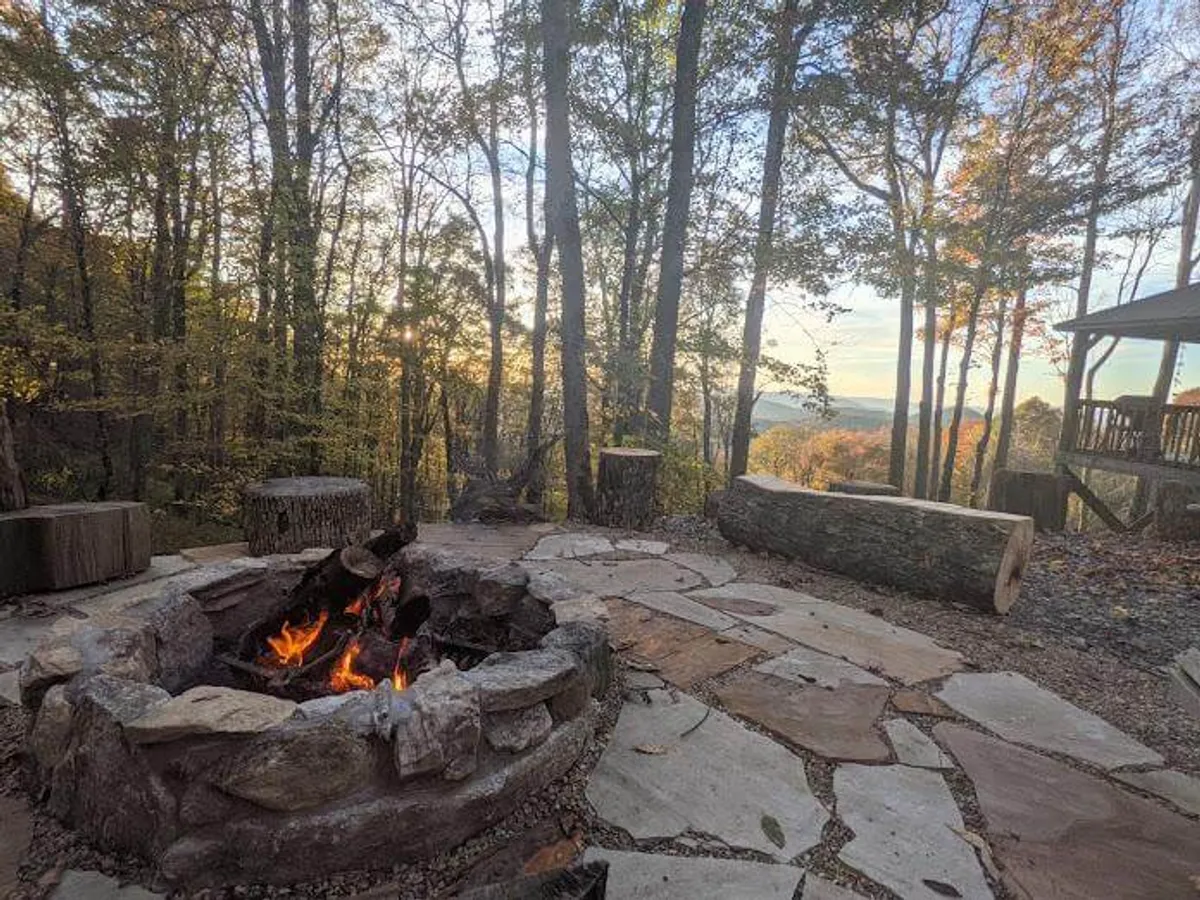 A cozy fire pit encircled by rustic log seating, with trees and a backdrop of distant mountains. The area is designed for gatherings, storytelling, and stargazing, inviting guests to create lasting memories outdoors.