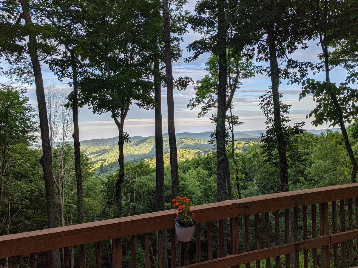 A view from the deck featuring distant mountains, lush greenery, and a flower pot on the railing. The tranquil scene suggests enjoying nature views, relaxing, or meditating, with the open sky inviting guests to linger at any time of day.