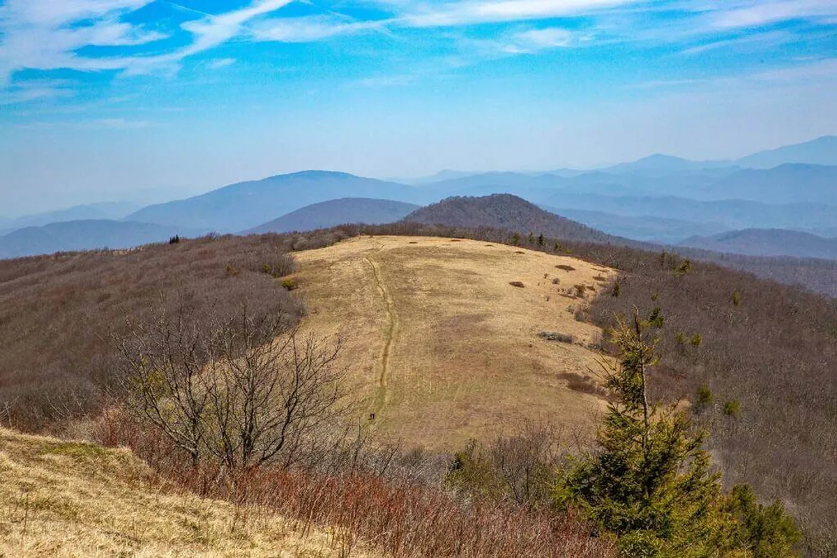 An expansive mountain range stretches across the horizon, with an open field in the foreground and a vast, serene sky overhead. The untouched landscape beckons outdoor enthusiasts to set off on their next adventure, promising opportunities for hiking, photography, and nature observation.