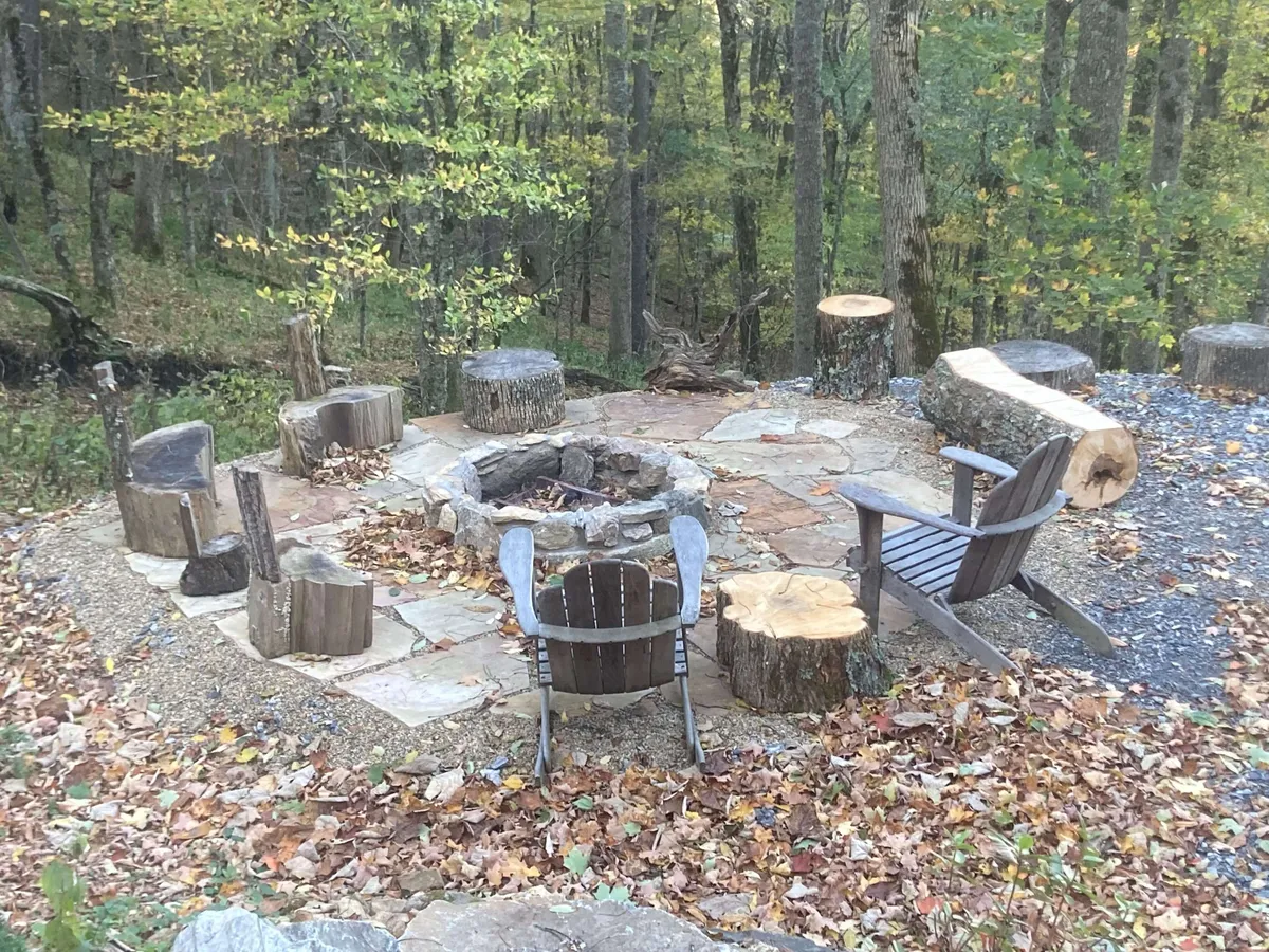 An inviting outdoor fire pit with rustic wooden seating, surrounded by forest. The scene suggests warmth, communal storytelling, and stargazing opportunities under clear mountain skies.