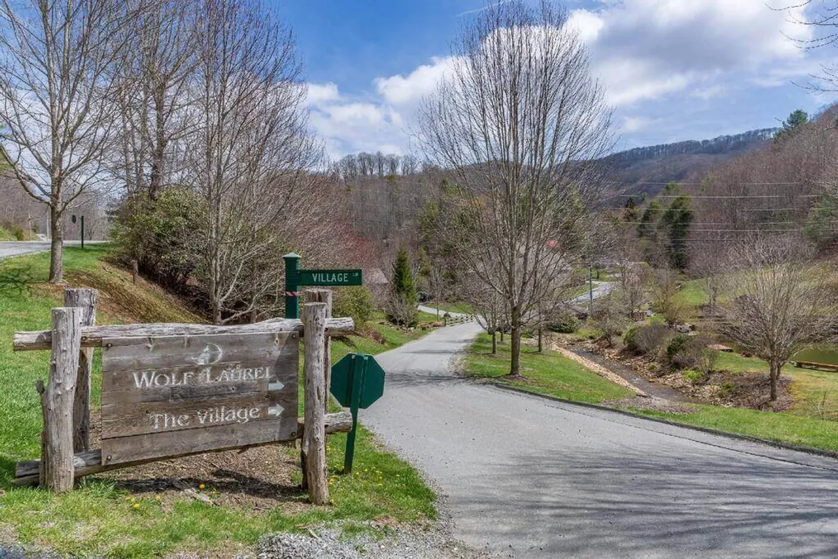 The welcoming entrance to Wolf Laurel Resort, marked by a rustic wooden sign and a scenic road winding into a lush, tree-lined village. This entryway invites guests to explore the amenities and natural beauty of the resort grounds.