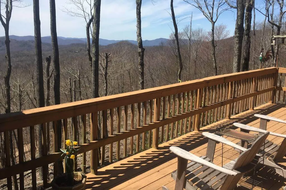 This image showcases a spacious wooden deck outfitted with potted flowers and comfortable wooden chairs, offering a sweeping view of the distant mountains. The scene is serene, capturing the tranquil atmosphere ideal for enjoying morning coffee, reading, or simply absorbing the natural beauty.