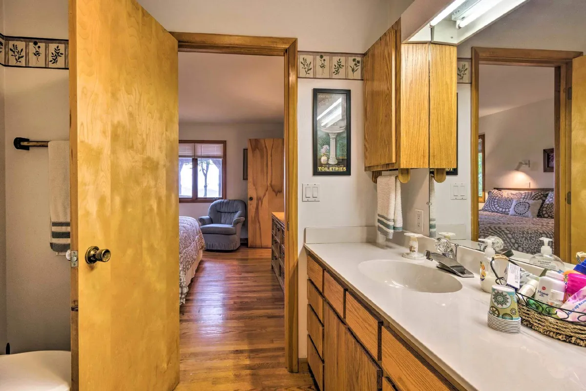 A well-appointed bathroom with wooden cabinetry, a large mirror, bathroom fixtures, and decorative items on the sink. The scene exudes a calm, cozy mood, suggesting a refreshing and comfortable experience for guests.