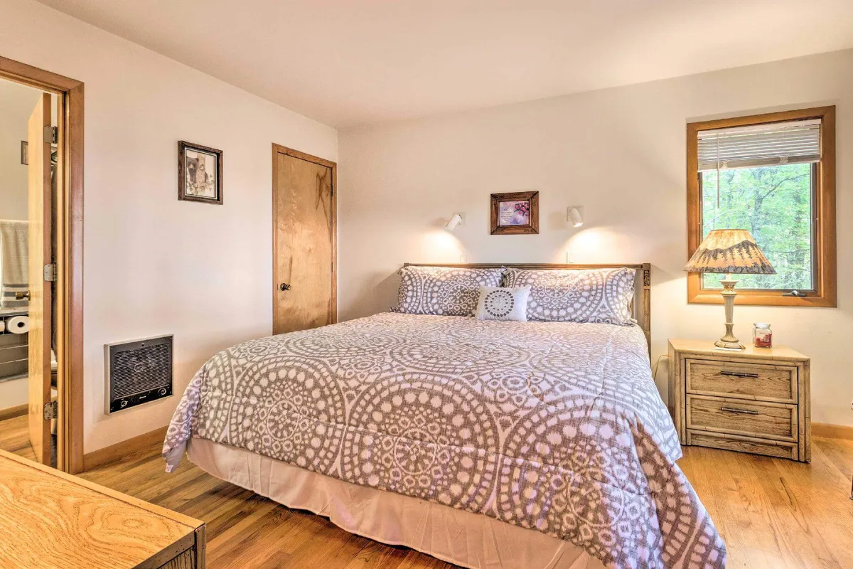 This image depicts a serene bedroom featuring a bed with patterned bedding, a nightstand with a lamp, and a window allowing natural light to filter in. The space feels relaxed and comforting, inviting restful moments after a day of adventure.